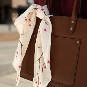 cream cherry blossom hand-embroidered scarf tied to a brown leather bag.