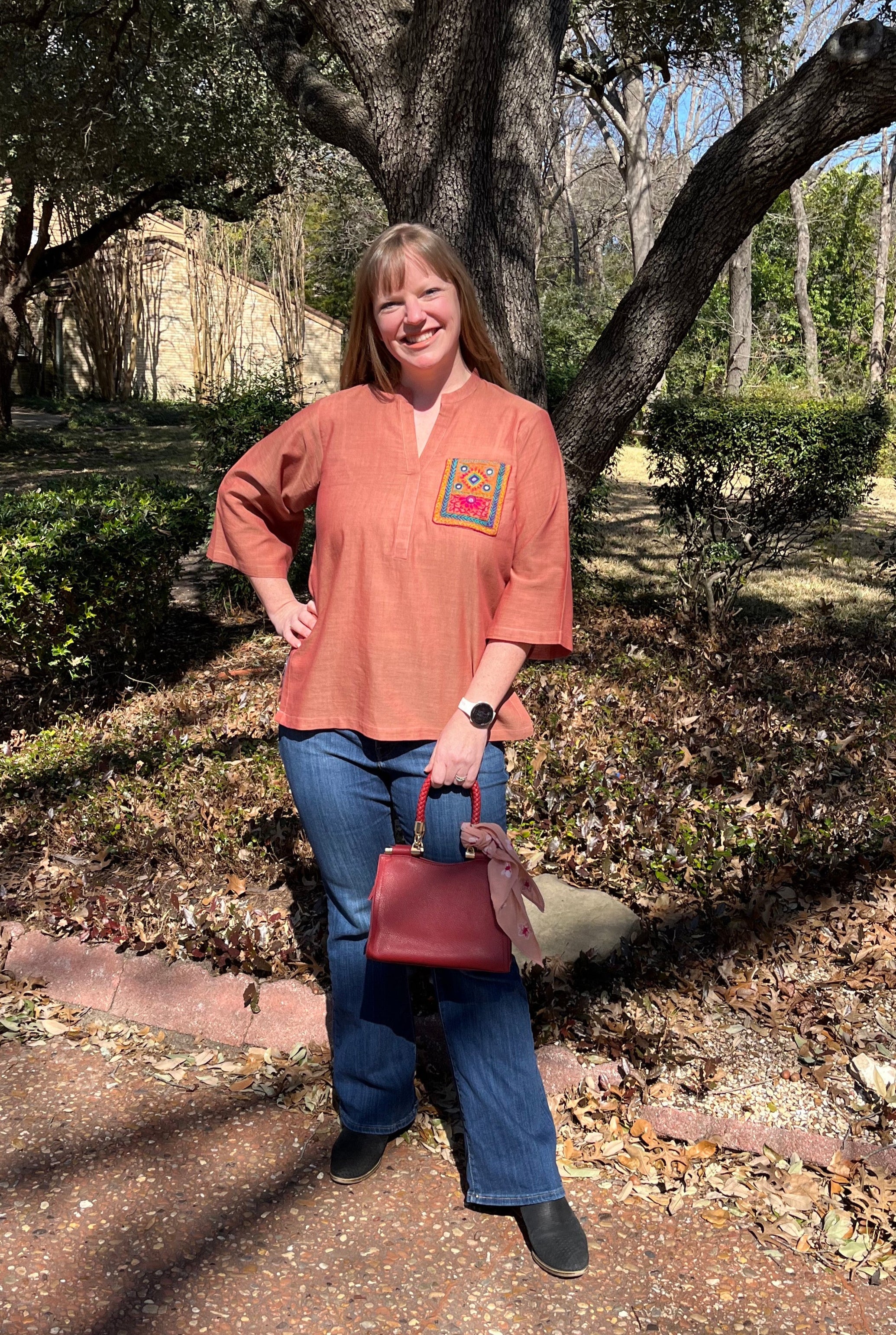 A person standing outdoors is wearing a pink cotton shirt with an embroidered pocket in pink and green color.