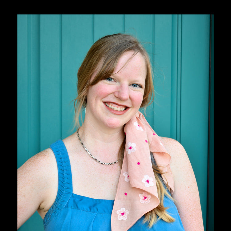 A woman wearing a blue dress with a hand-embroidered pink scrunchie scarf accessorized in her hair.